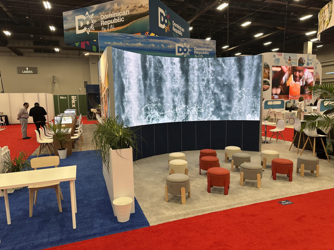 Exhibit with a curved LED waterfall display, lounge seating, and greenery on the show floor